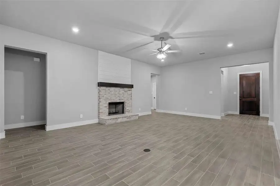 Unfurnished living room with light wood-type flooring, ceiling fan, and a brick fireplace