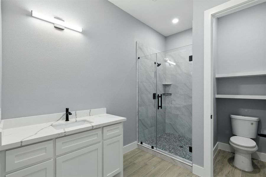 This modern bathroom features a sleek design with a glass-enclosed shower, tiled walls, and a stylish vanity with a marble countertop. The space is well-lit, offering a clean and fresh look.