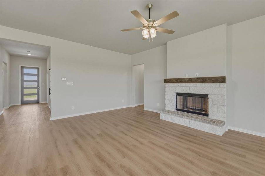 Spacious interior featuring wood-finish flooring, a contemporary ceiling fan, and a fireplace with a white stone surround and a wood mantel Spacious interior featuring wood-finish flooring, a contemporary ceiling fan, and a fireplace with a white stone surround and a wood mantel