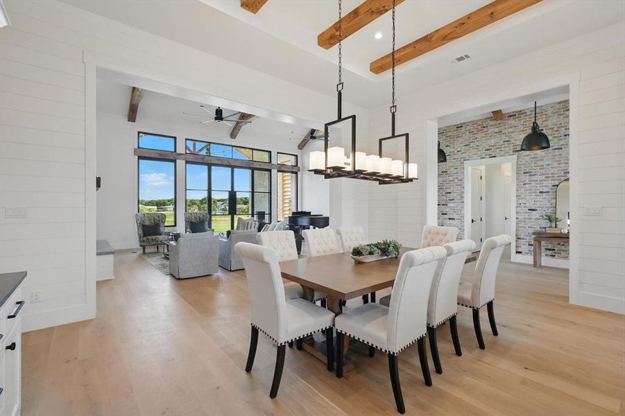 Dining area featuring beamed ceiling, light wood finished floors, ceiling fan, a chandelier, and a towering ceiling Dining area featuring beamed ceiling, light wood finished floors, ceiling fan, a chandelier, and a towering ceiling