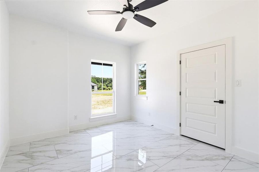 Spacious room featuring large format tile flooring, white walls, and a modern ceiling fan with dark blades