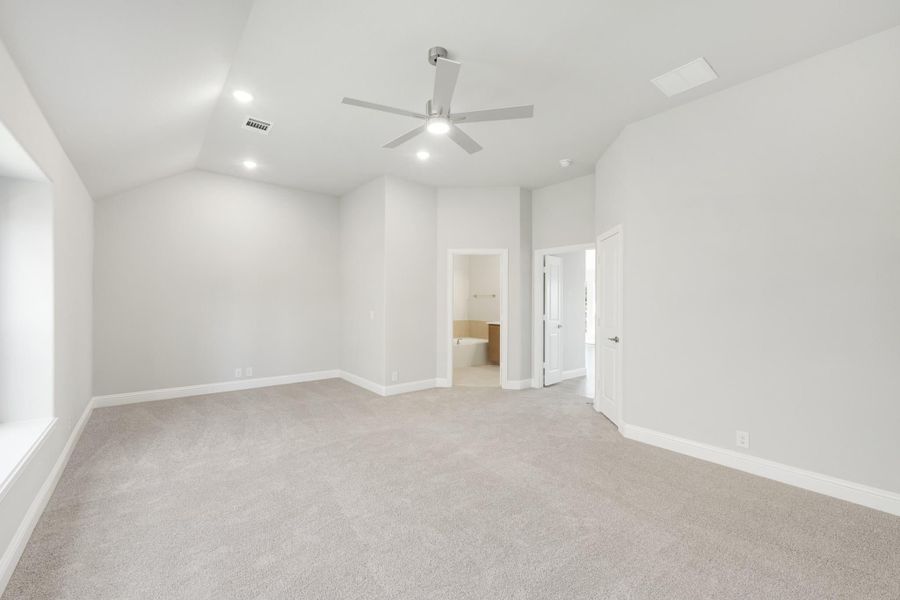 Empty bedroom with vaulted ceiling, ceiling fan, carpet flooring, and ensuite bathroom doorway