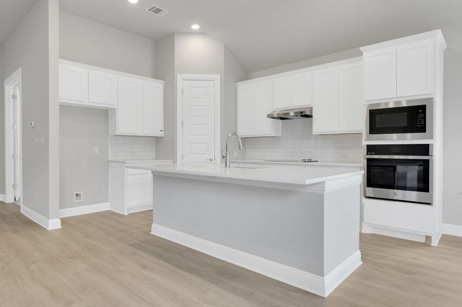 Kitchen with stainless steel oven, tasteful backsplash, a center island with sink, light countertops, and white cabinetry
