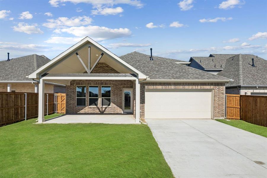 Rear view of property featuring brick siding, a patio area, driveway, roof with shingles, and a garage