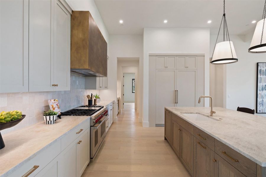 Kitchen featuring light wood finished floors, a sink, tasteful backsplash, double oven range, and custom exhaust hood Kitchen featuring light wood finished floors, a sink, tasteful backsplash, double oven range, and custom exhaust hood