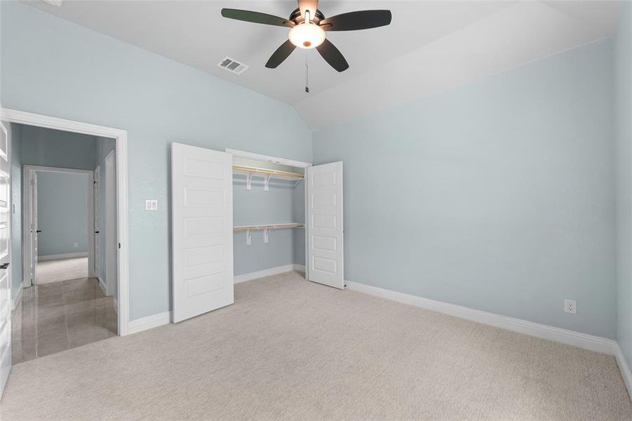 Unfurnished bedroom featuring vaulted ceiling, a closet, carpet floors, and ceiling fan