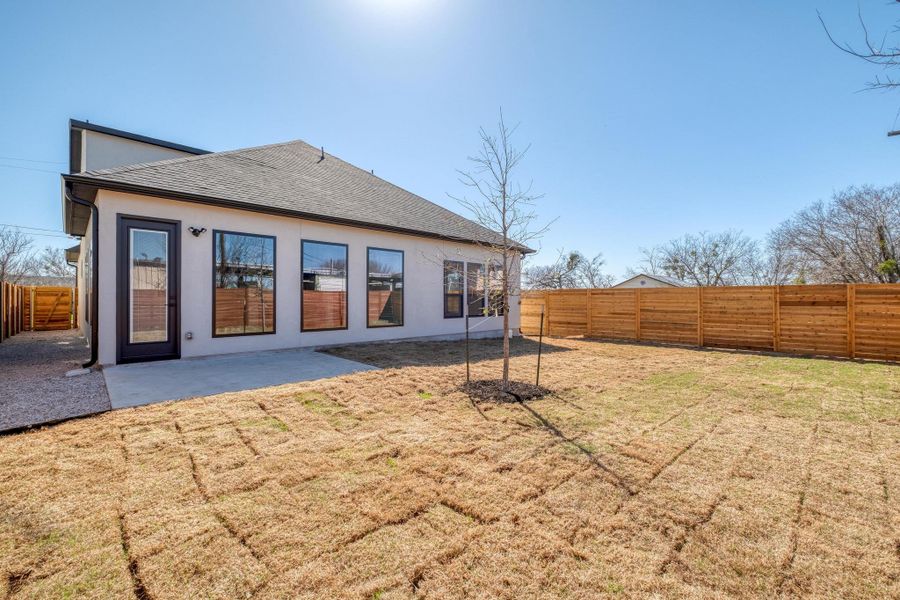 Back of property featuring roof with shingles, stucco siding, a yard, a fenced backyard, and a patio