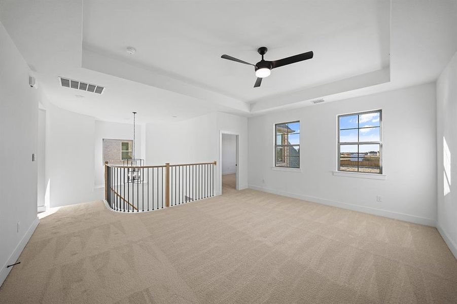 Empty room with a tray ceiling, light carpet, and a ceiling fan