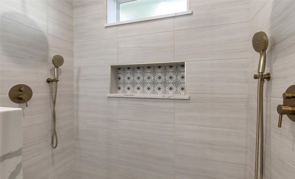 Primary shower, featuring elegant dual showerheads, chic modern tiling, and a stylish recessed shelf for added convenience.