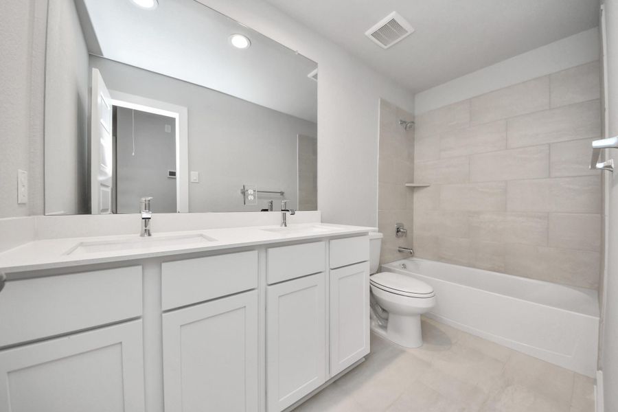 Secondary bath features tile flooring, bath/shower combo with tile surround, light stained wood cabinets, beautiful light countertop.