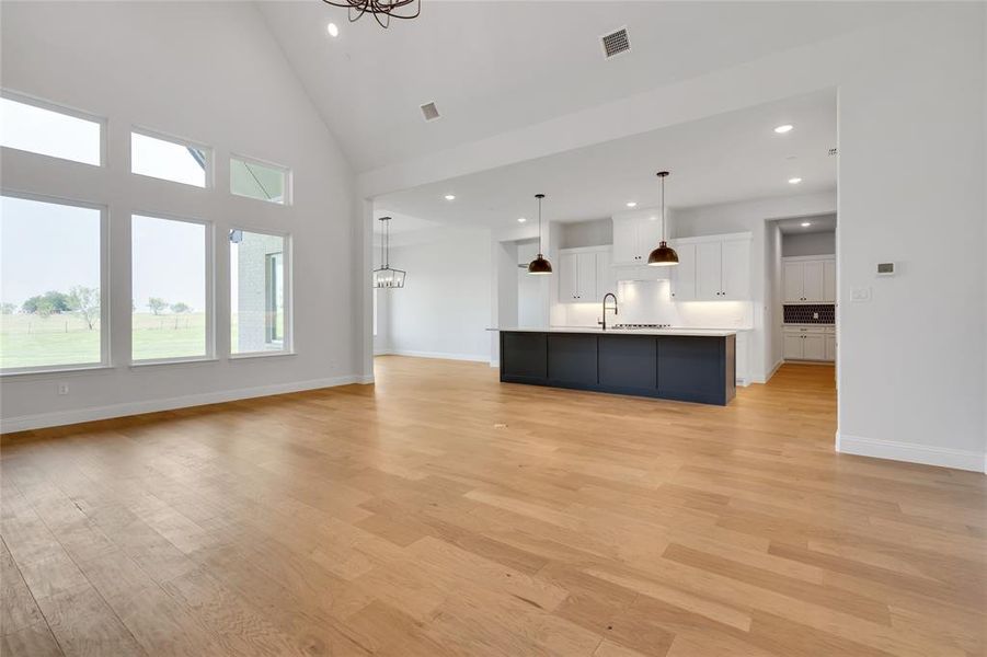 Unfurnished living room featuring high vaulted ceiling, an inviting chandelier, sink, and light hardwood / wood-style floors