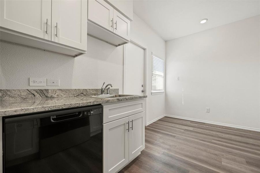 Kitchen featuring dishwasher, wood-like flooring, white cabinetry, and light stone counters