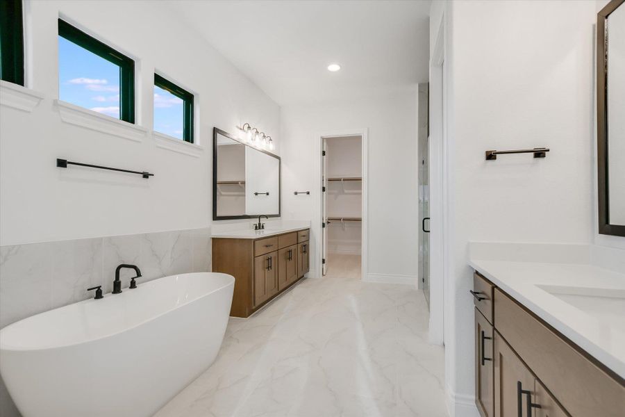 Full bath featuring marble tiled flooring, two vanities, a freestanding bath, a walk in closet, and recessed lighting