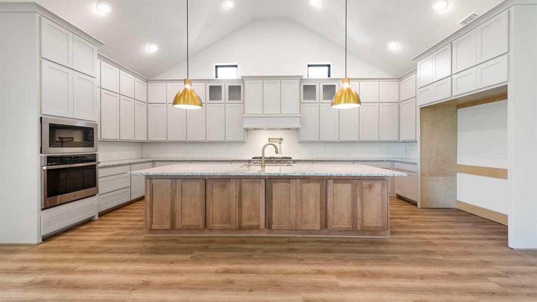 Kitchen with light hardwood / wood-style floors, oven, black microwave, and high vaulted ceiling