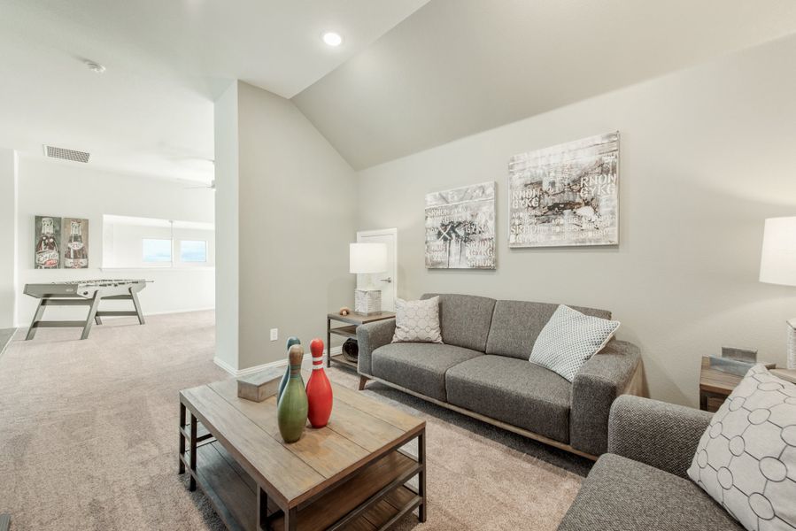 Bonus room with gray sofa, vaulted ceiling, carpet flooring, and foosball table in background