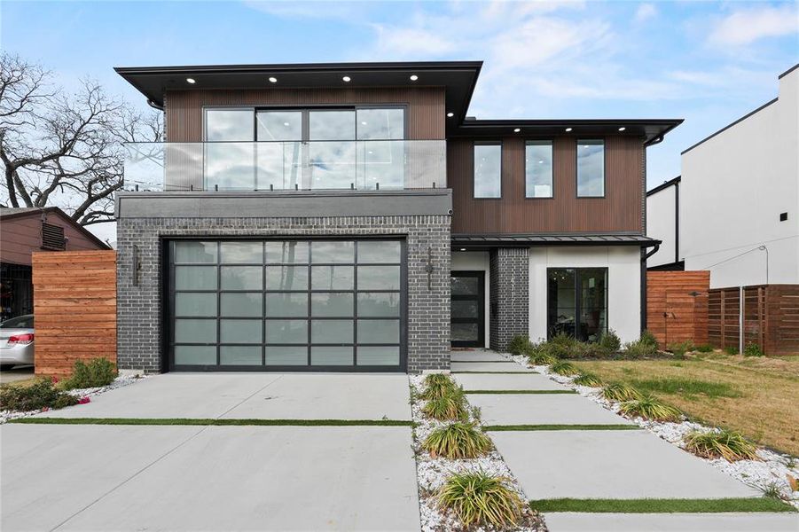 Contemporary home featuring driveway, brick siding, a metal roof, and an attached garage Contemporary home featuring driveway, brick siding, a metal roof, and an attached garage