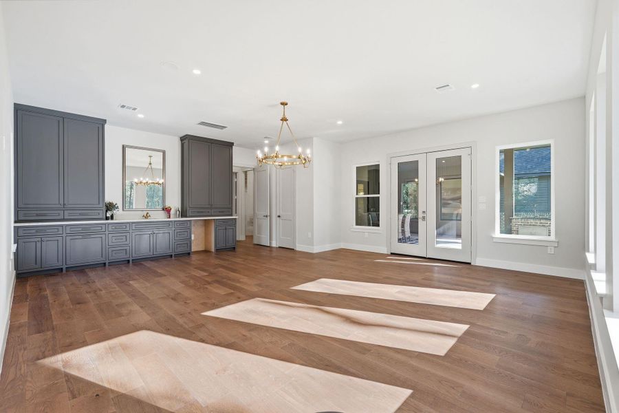 A spacious game room designedfor hosting, featuring a stylishwet bar with custom cabinetry,prep counter, sink and built-inbeverage fridge, all anchored bya statement chandelier and richwood floors.