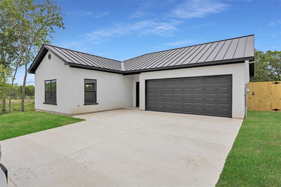 Modern inspired farmhouse with a standing seam roof, concrete driveway, a metal roof, and an attached garage