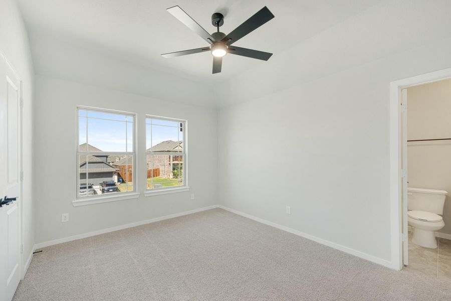 Empty bedroom with carpet, ceiling fan, two windows, and an attached bathroom visible through open door Empty bedroom with carpet, ceiling fan, two windows, and an attached bathroom visible through open door