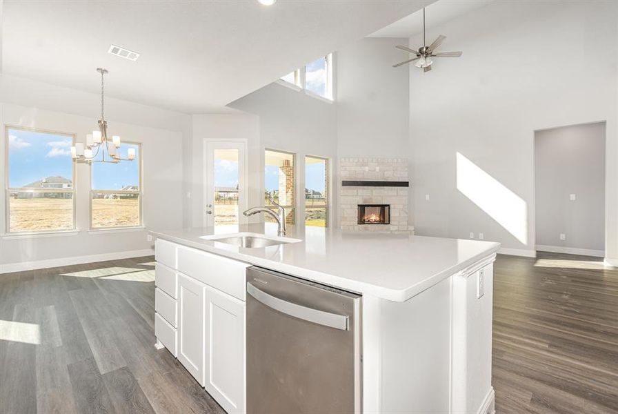 Kitchen featuring an island with sink, open floor plan, stainless steel dishwasher, a towering ceiling, and white cabinetry