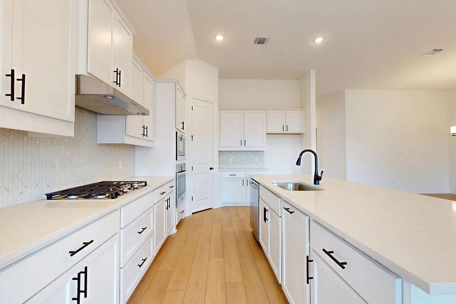 The kitchen features white cabinetry with black hardware, light-colored countertops, and hardwood flooring