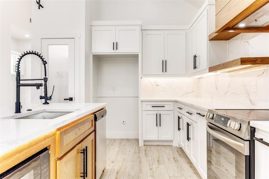 Kitchen with white cabinets, appliances with stainless steel finishes, light stone countertops, light wood-style floors, and tasteful backsplash Kitchen with white cabinets, appliances with stainless steel finishes, light stone countertops, light wood-style floors, and tasteful backsplash