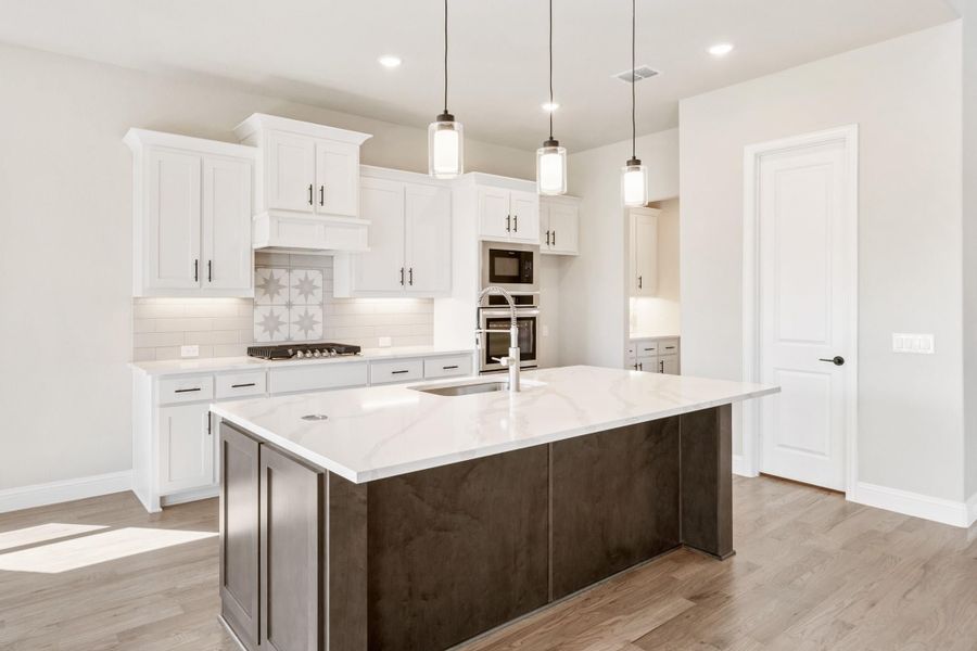 Kitchen with white cabinets, large dark island with quartz countertop, pendant lights, and stainless steel appliances