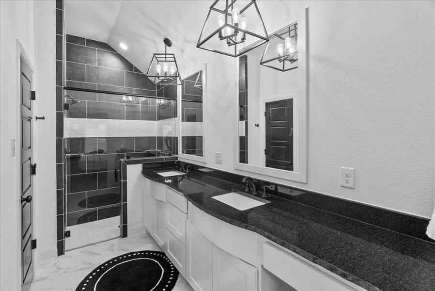 Bathroom featuring a shower stall, double vanity, an inviting chandelier, marble finish floor, and a sink