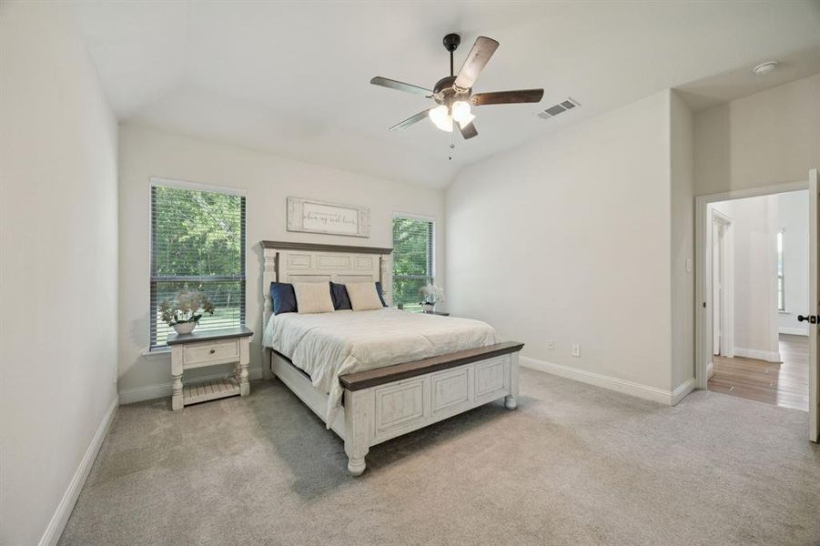 Master bedroom featuring serene views of the property, light colored carpet, neutral paint, multiple windows, and ceiling fan.