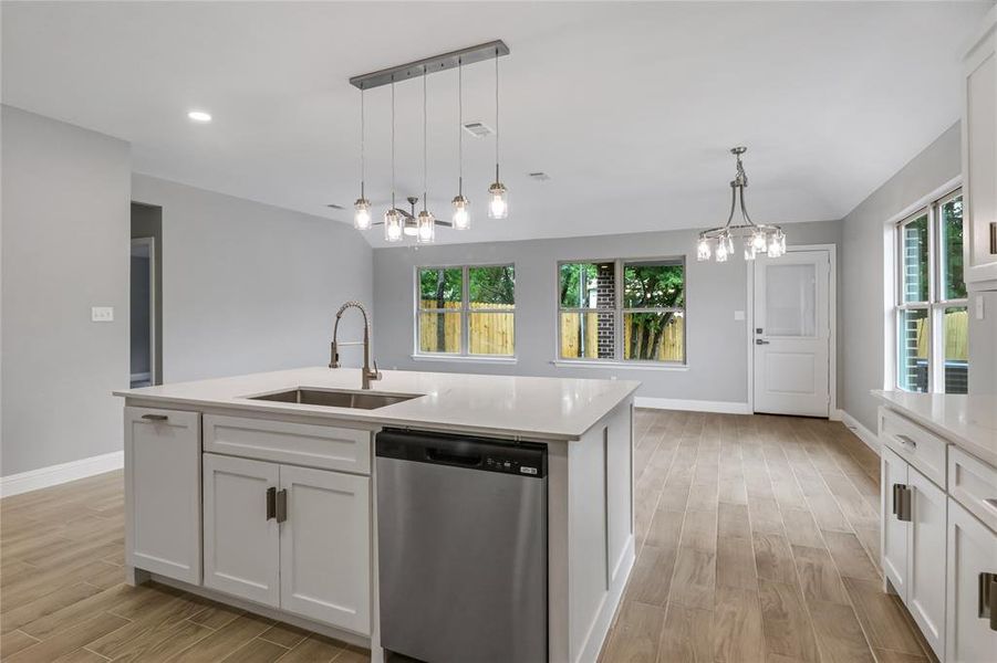 Kitchen with sink, light hardwood / wood-style floors, stainless steel dishwasher, an island with sink, and white cabinetry