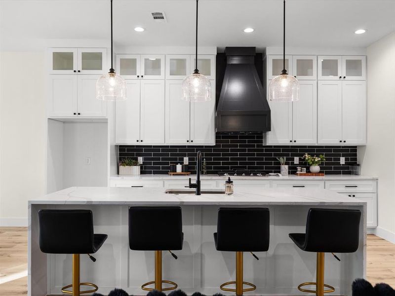 Kitchen featuring light wood finished floors, glass insert cabinets, a kitchen bar, and light stone countertops