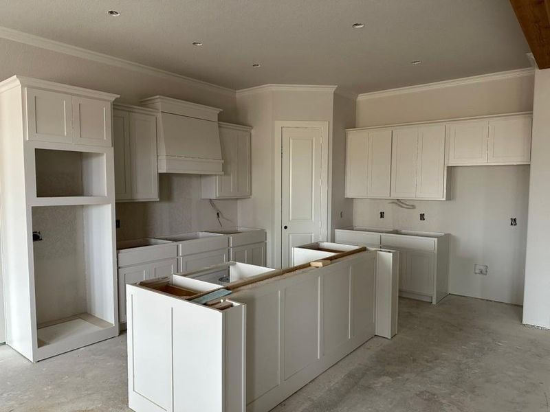 Kitchen with a center island, ornamental molding, white cabinetry, and unfinished concrete flooring