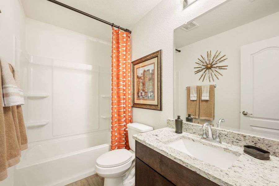 Bathroom with granite vanity, dark wood cabinets, and tub with orange shower curtain