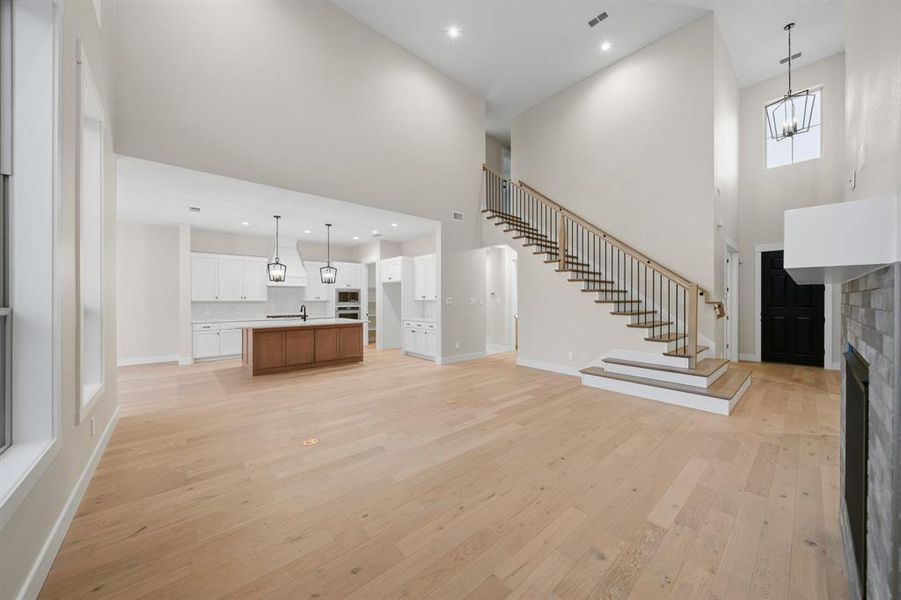 Unfurnished living room featuring light wood-type flooring, a fireplace, a high ceiling, stairway, and recessed lighting
