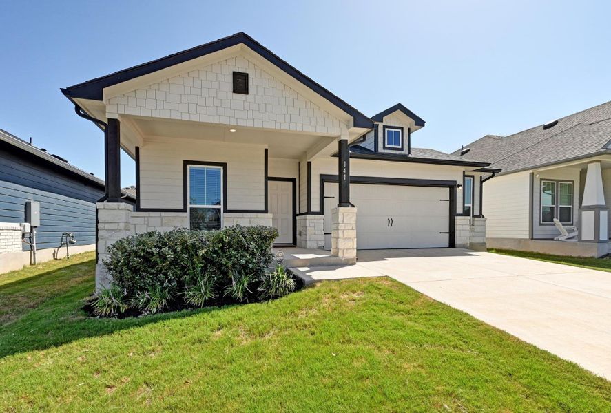 View of front of property with concrete driveway, stone siding, a front yard, and a garage