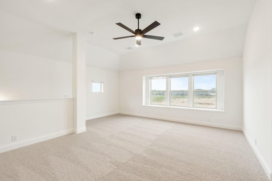 Empty bedroom with beige carpet, ceiling fan, and large windows overlooking a yard