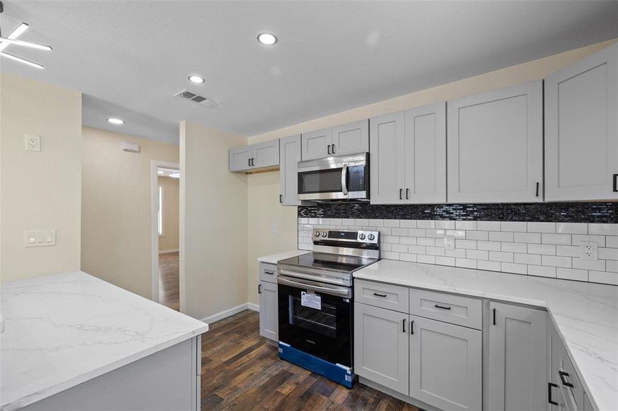 Kitchen with electric stove, tasteful backsplash, dark wood-type flooring, light stone countertops, and gray cabinetry