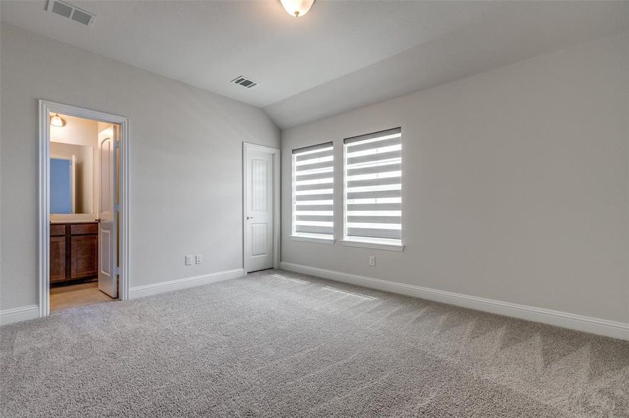 Unfurnished bedroom featuring light carpet, baseboards, lofted ceiling, and ensuite bathroom