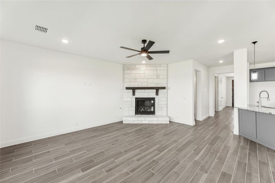 Open living room with white brick fireplace, ceiling fan, and wood-look tile floors Open living room with white brick fireplace, ceiling fan, and wood-look tile floors