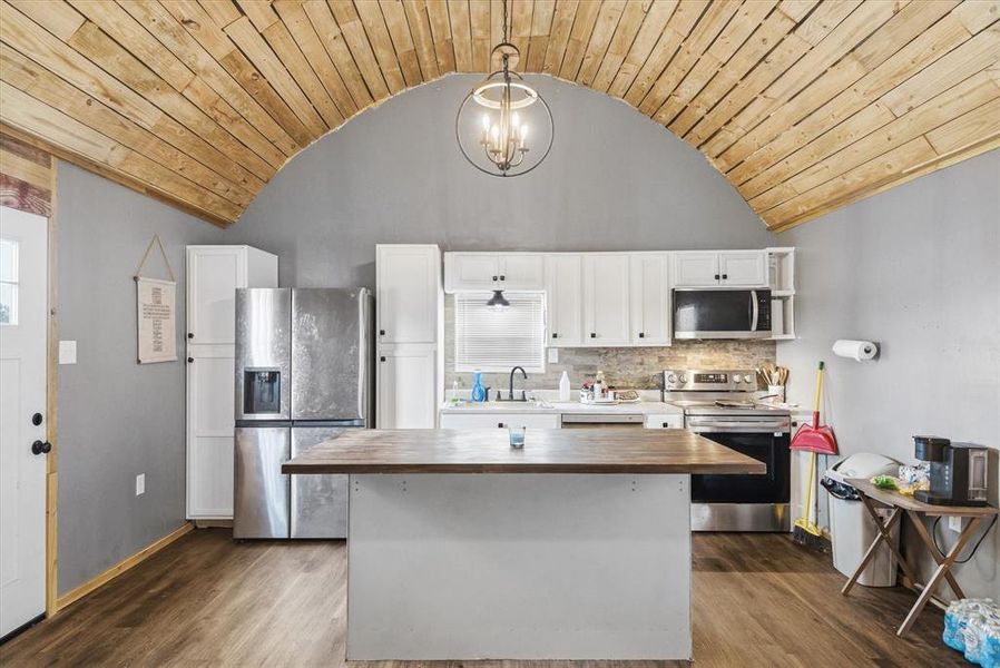 Kitchen featuring wood counters, stainless steel appliances, white cabinets, hanging lights, and a center island