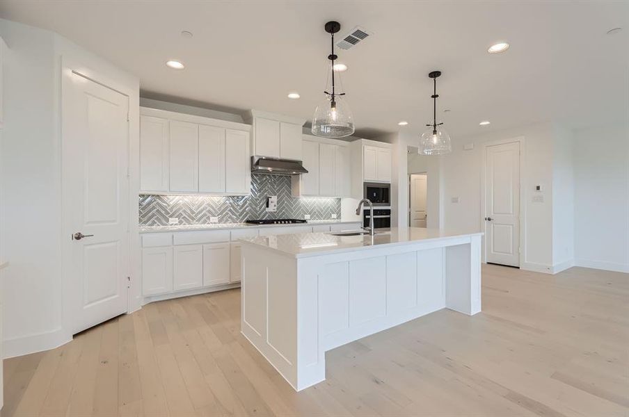 Kitchen featuring white cabinets, appliances with stainless steel finishes, hanging light fixtures, and an island with sink