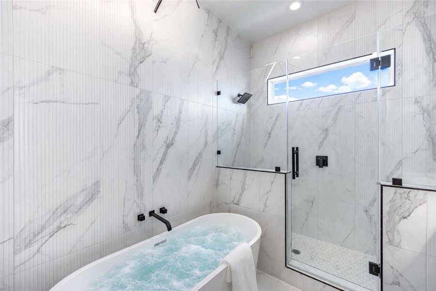 Primary bathroom featuring double vanity sinks with quartz countertops, adjustable anti-fog mirrors, and tile flooring. Highlights include 10-ft ceilings, a freestanding soaking tub, chandelier accent lighting, and a frameless shower with floor-to-ceiling tile.