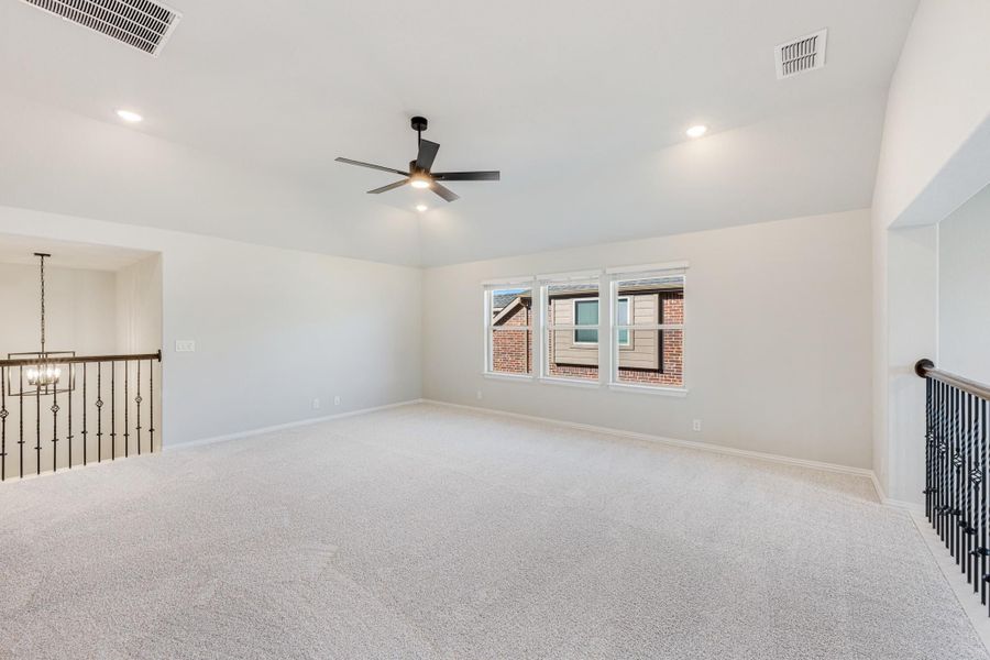 Open upstairs loft with carpet flooring, ceiling fan, and iron stair railing Open upstairs loft with carpet flooring, ceiling fan, and iron stair railing