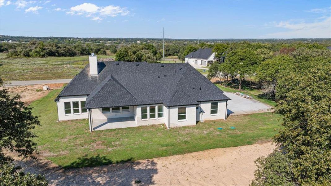 Aerial perspective showcasing a modern single-story residence Backside with a dark shingle roof and light-colored stone and siding exterior