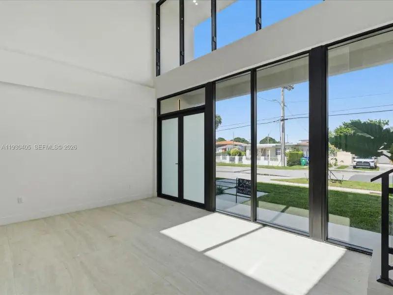 Double-height ceiling, floor-to-ceiling windows with black frames, tile flooring, and frosted glass paneled door Double-height ceiling, floor-to-ceiling windows with black frames, tile flooring, and frosted glass paneled door