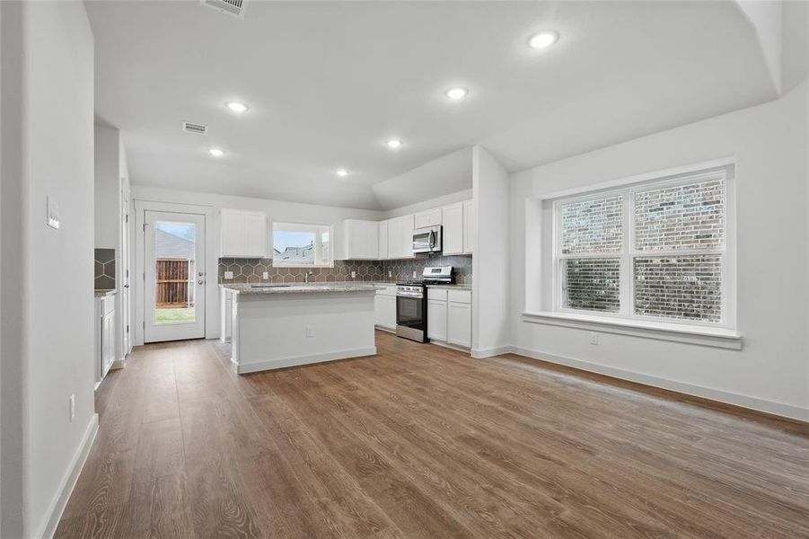 Kitchen featuring white cabinetry, wood finished floors, appliances with stainless steel finishes, and decorative backsplash Kitchen featuring white cabinetry, wood finished floors, appliances with stainless steel finishes, and decorative backsplash