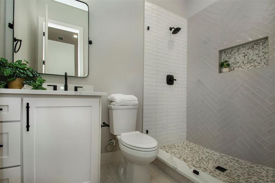 Bathroom featuring tiled shower, vanity, and toilet