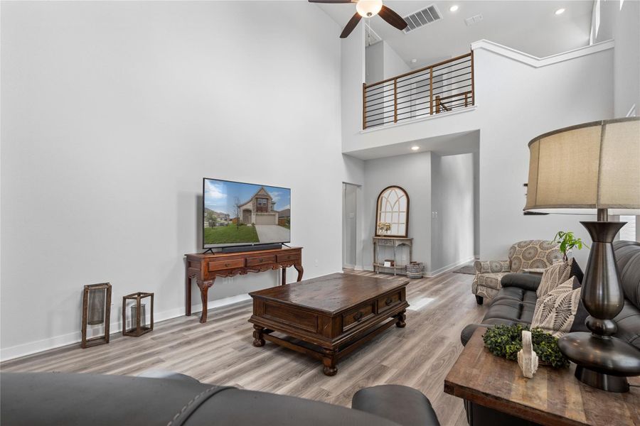 Living room featuring wood finished floors, a ceiling fan, a high ceiling, baseboards, and recessed lighting Living room featuring wood finished floors, a ceiling fan, a high ceiling, baseboards, and recessed lighting