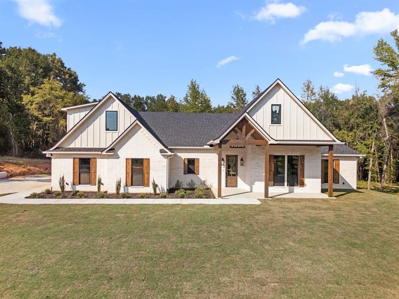 Modern inspired farmhouse with board and batten siding, brick siding, covered porch, a front lawn, and roof with shingles