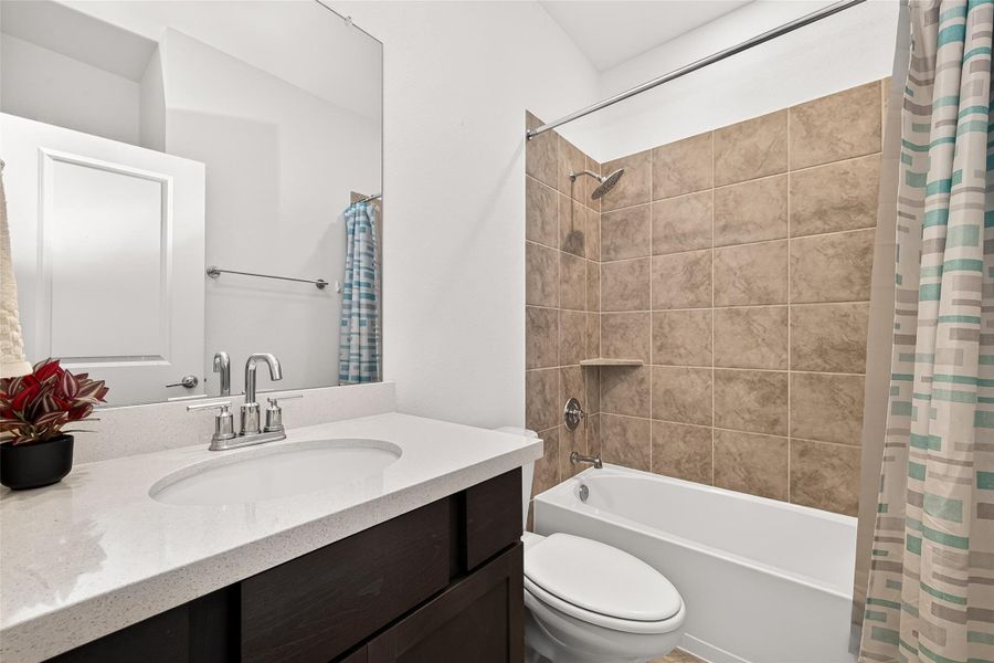 Secondary downstairs bathroom featuring quartz countertops, dark cabinetry, and a tub/shower combination with tile surround. Conveniently located on the first floor with neutral finishes and functional design.